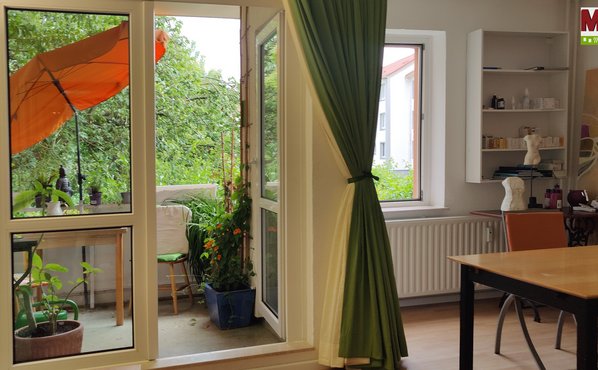 Balkon, orangen Sonnenschirm, rechts im Bild der Esstisch