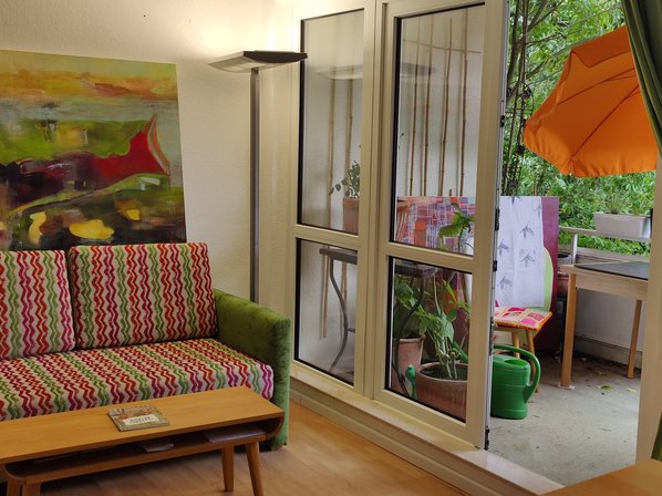 Links im Bild die Couch, darüber ein großes Bild, Lampe und Balkon rechts